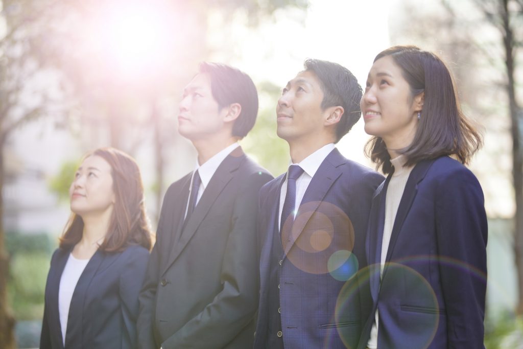 太陽光を浴びるスーツを着た4人が